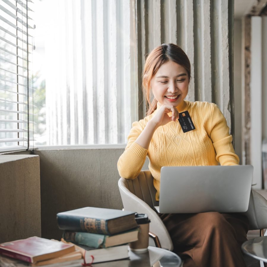 Asian woman holding a credit card and using a laptop computer Businesswoman working at modern office, online shopping, ecommerce, internet banking, spending money, credit card working concept.